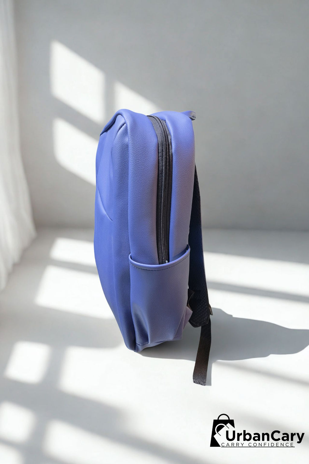 A light blue backpack standing upright on a white floor with strong window shadows, shown from the side. The backpack has a side pocket and a black strap hanging from the bottom. Mens Leather Backpack