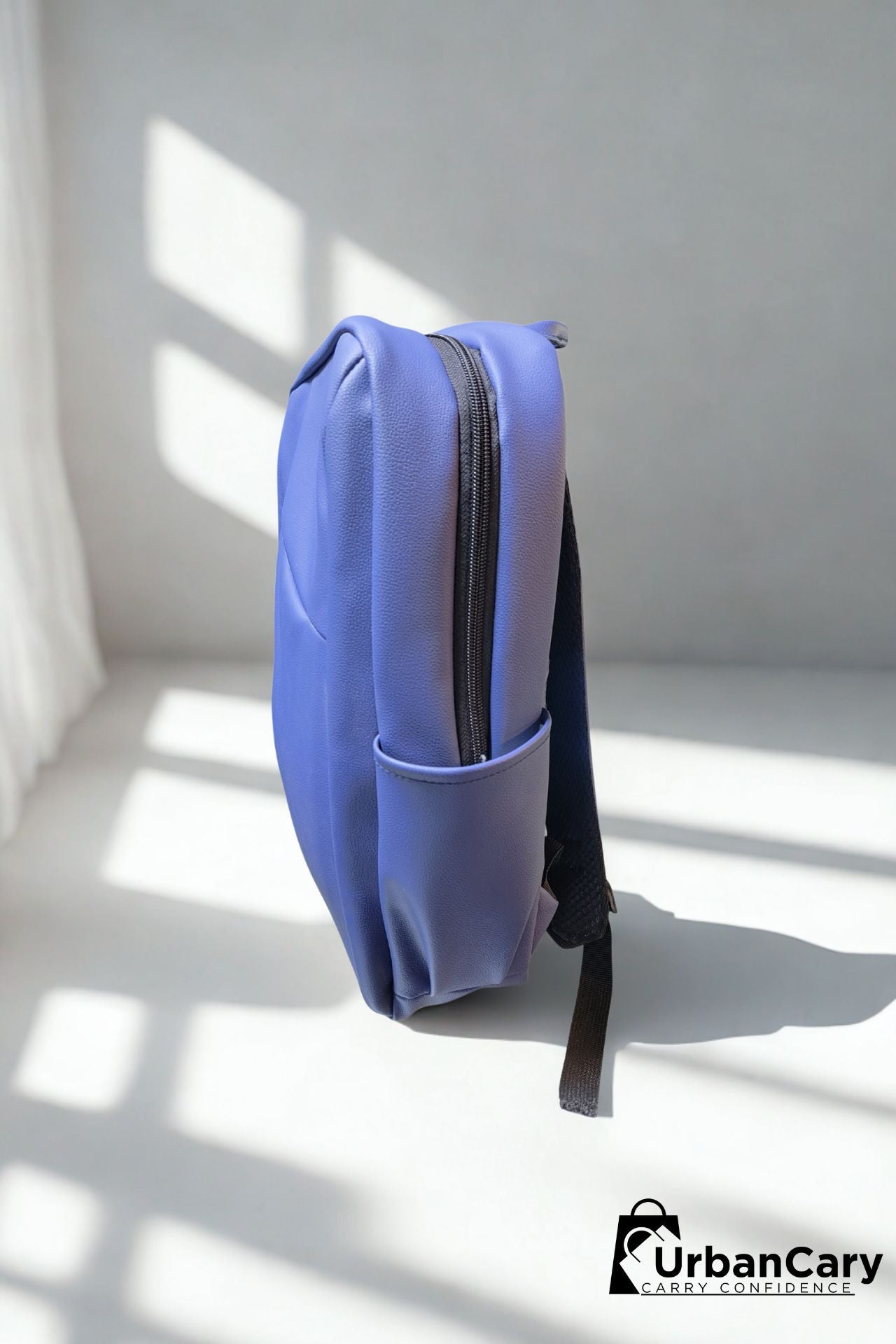 A light blue backpack standing upright on a white floor with strong window shadows, shown from the side. The backpack has a side pocket and a black strap hanging from the bottom. Mens Leather Backpack